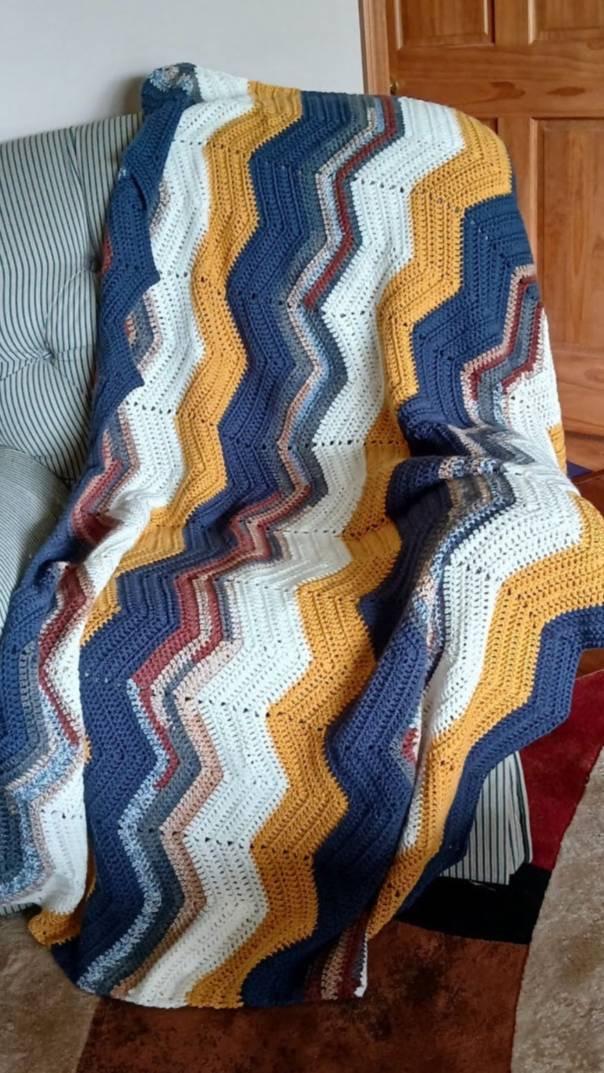 Colorful crocheted blanket draped over a chair in a room with wooden flooring.
